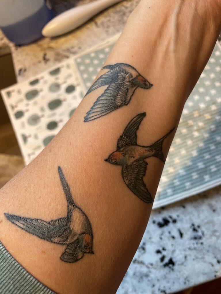 Three barn swallow tattoos on a forearm, each bird representing a year of sobriety in a meaningful midlife tattoo.