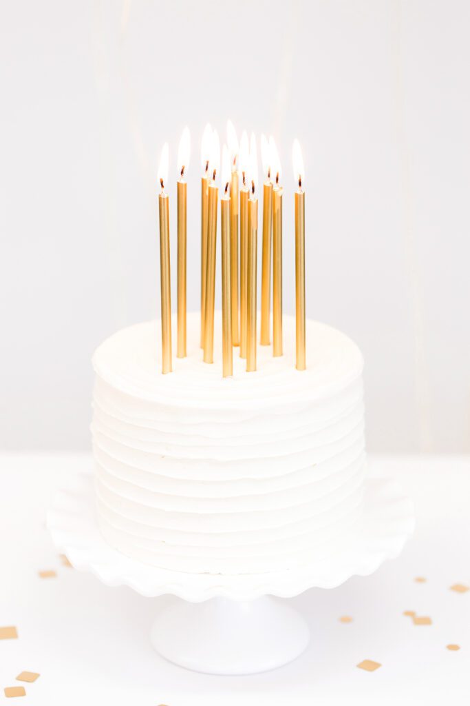 white birthday cake with gold pillar candles